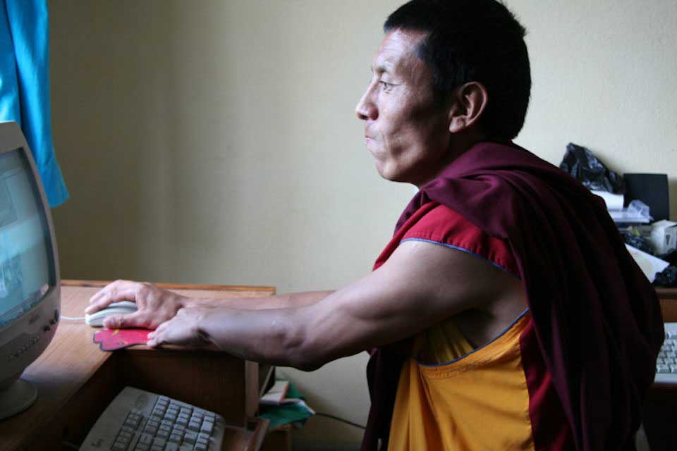 older man wearing orange and red shirt on desktop computer