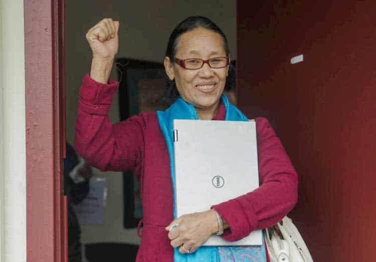 older woman holding laptop with her arm raised