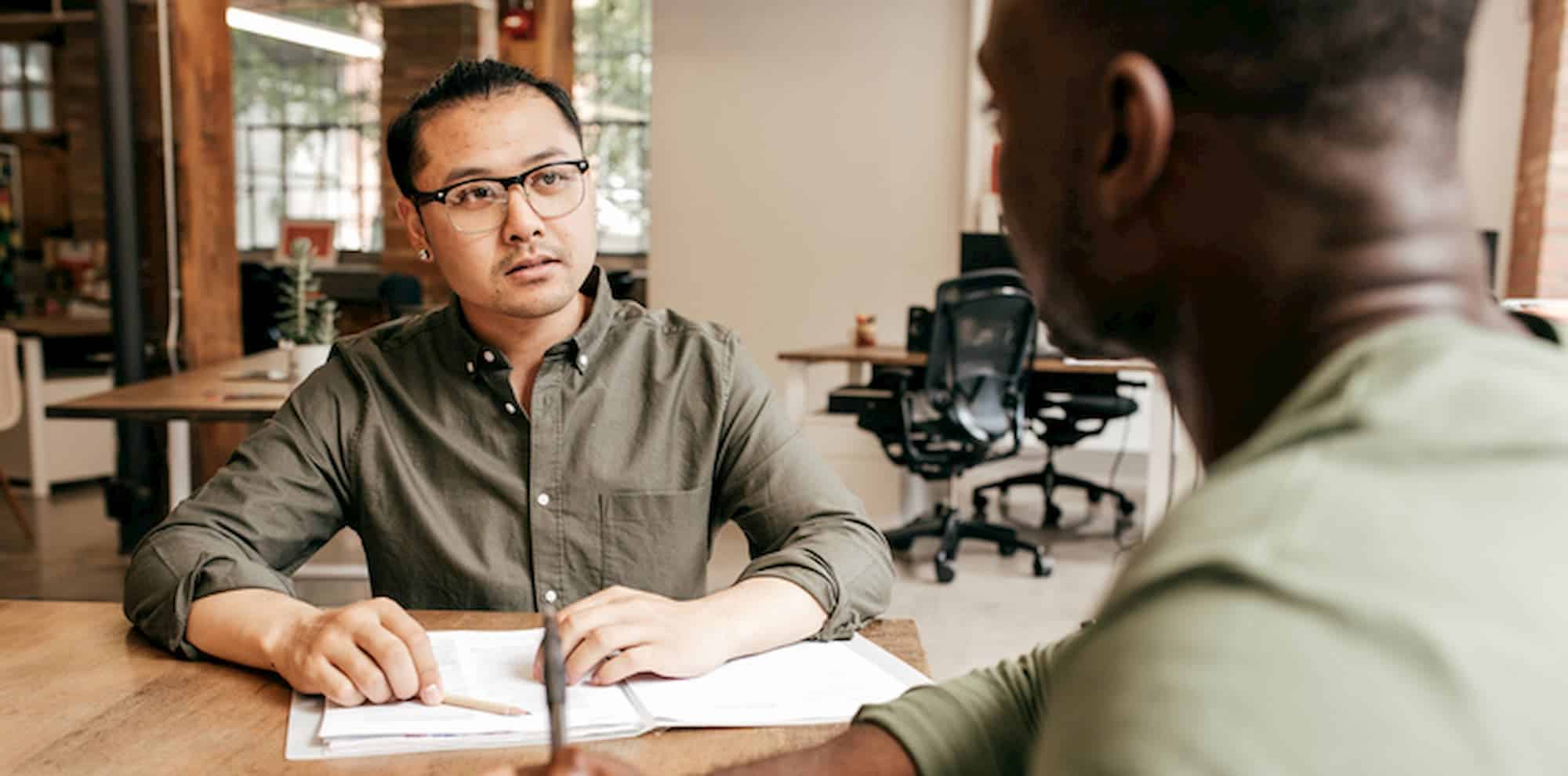 two men consulting at table in large workspace