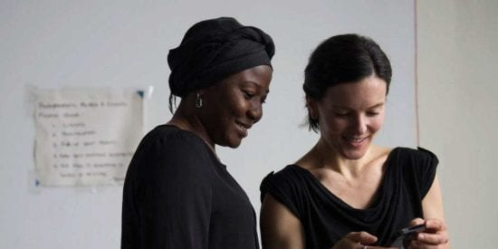 Two women are looking at a cellphone and smiling