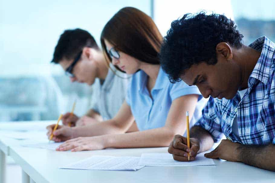 Tres jóvenes estudiantes adultos escribiendo en una mesa de clase